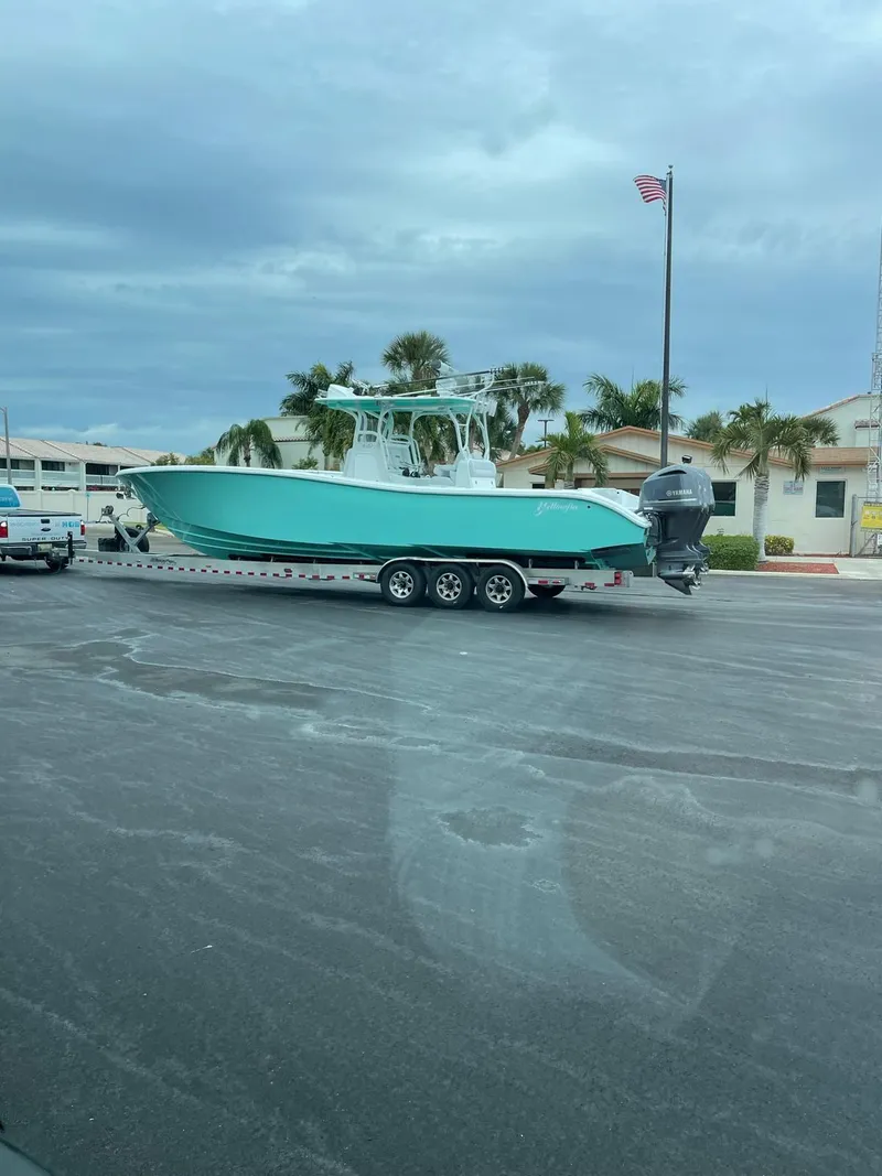 Slide: The Image of 2018 Yellowfin 36 boat on trailer, parked near palm trees and buildings. - 16