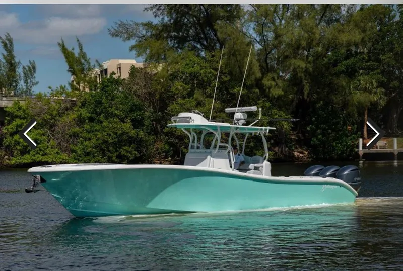 Slide: The Image of 2018 Yellowfin 36 boat on water, turquoise hull, triple engines, lush greenery background. - 4