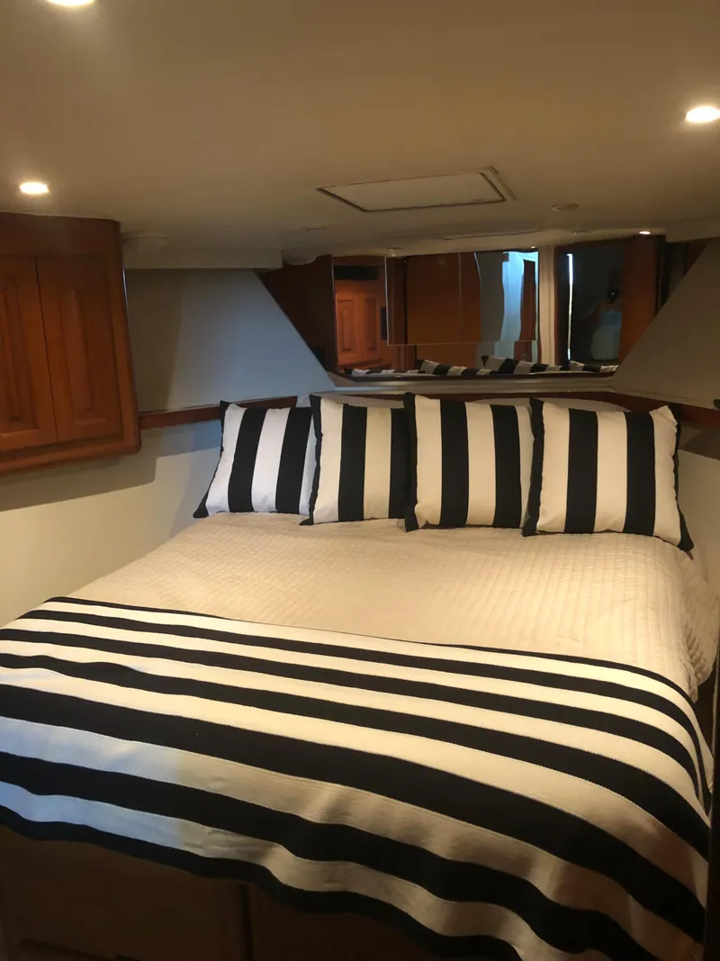 Slide: The Image of 1998 Viking 43 Convertible yacht bedroom with striped bedding and wooden cabinets. - 15