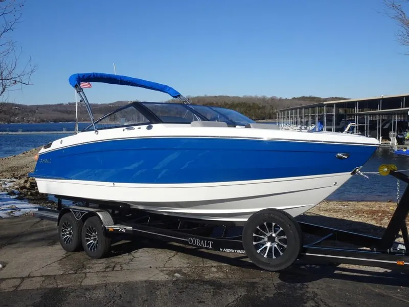 The Image of 2025 Cobalt R4 boat on trailer by a lake, featuring a blue and white design. - 1