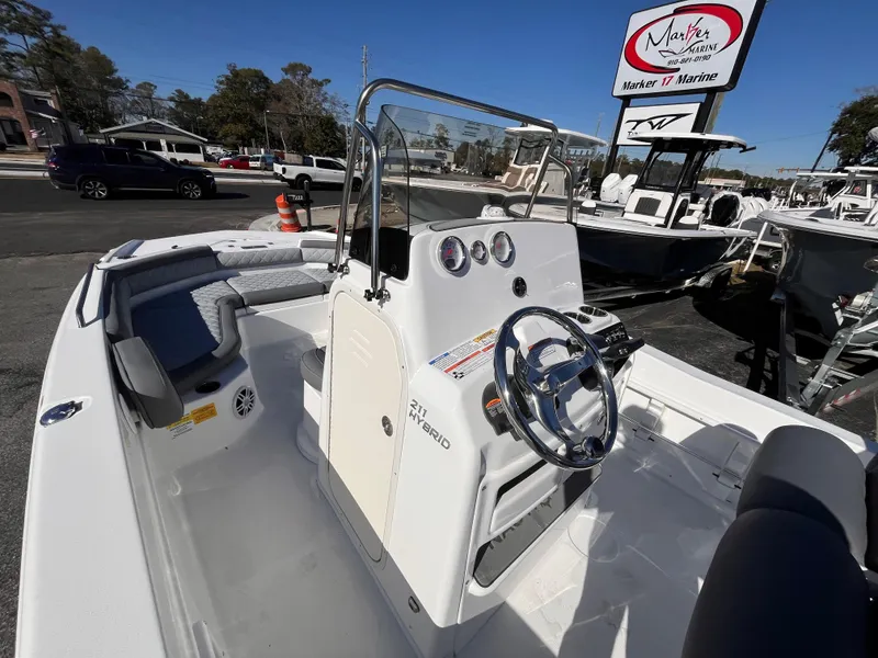 Slide: The Image of 2025 NauticStar 211 Hybrid boat, white interior, steering console, parked at a marina. - 13