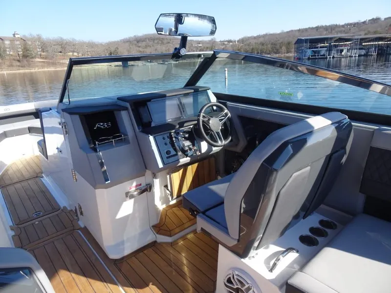 Slide: The Image of Cobalt R33 Surf 2025 boat interior with modern dashboard and steering, docked on a serene lake. - 18