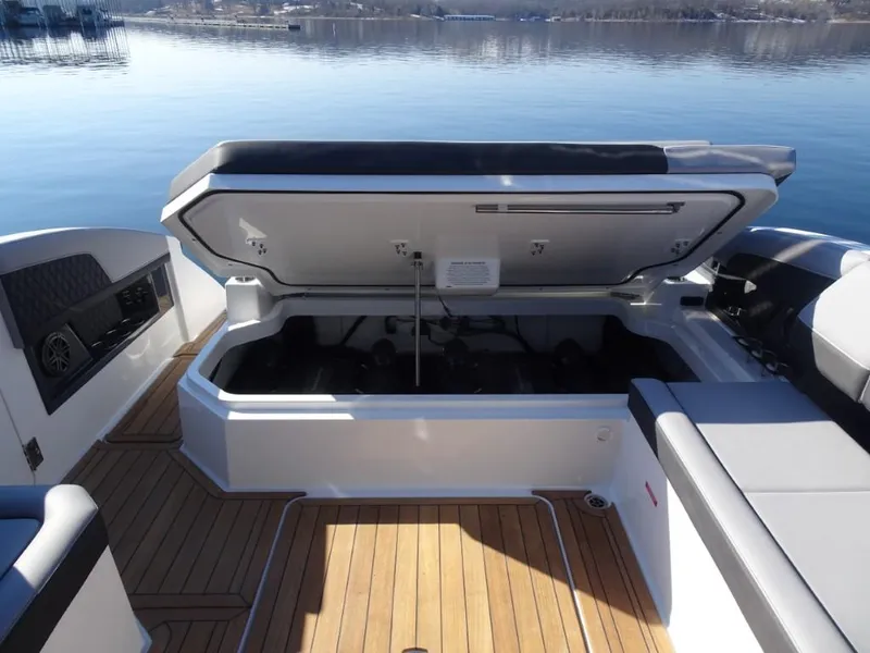 Slide: The Image of 2025 Cobalt R33 Surf boat with open storage compartment, wooden deck, and lake view. - 32