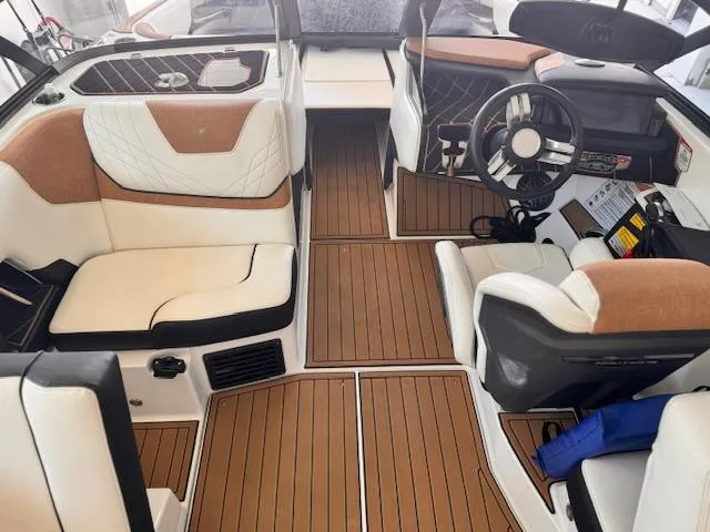 Slide: The Image of 2021 Nautique Super Air Nautique GS24 interior with tan and white seating, wood flooring, and steering console. - 26