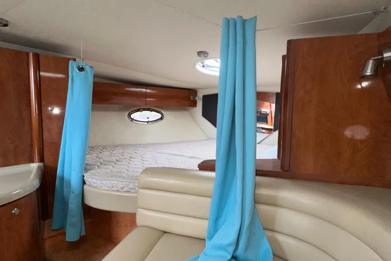 Slide: The Image of 2006 Larson Cabrio 350 cabin interior with bed, blue curtains, and wood paneling. - 26