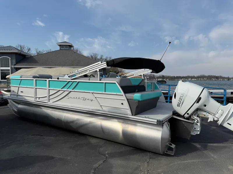 Slide: The Image of 2025 South Bay S222CR2 pontoon boat with teal accents, parked near a lake. - 29