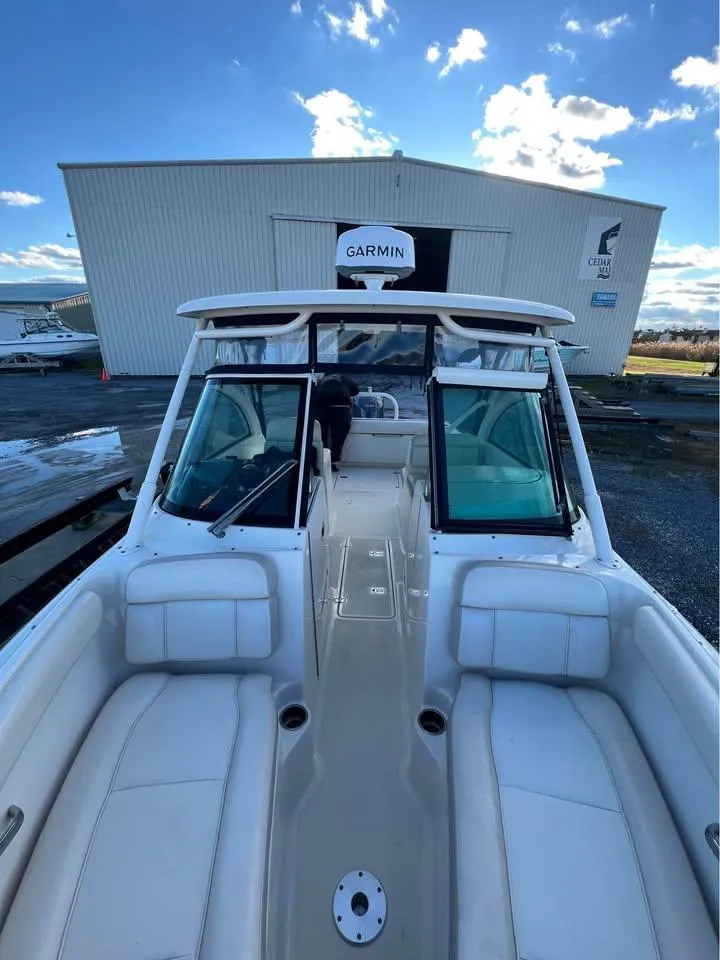 Slide: The Image of 2014 Pursuit DC 265 Dual Console boat with white seating, docked near a warehouse. - 18