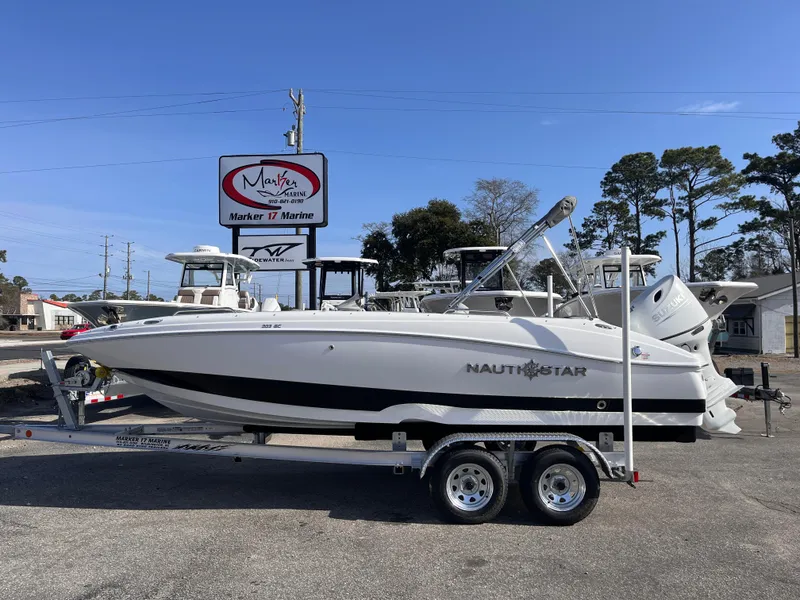 The Image of 2025 NauticStar 203 SC Deck boat on trailer at marina, clear sky background. - 0