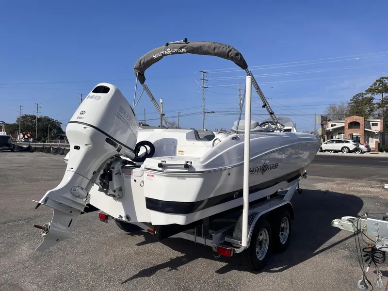 Slide: The Image of 2025 NauticStar 203 SC Deck boat on trailer, featuring outboard motor, parked outdoors. - 4