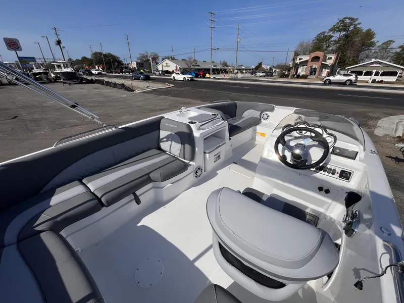 Slide: The Image of 2025 NauticStar 203 SC Deck boat interior with seating and steering wheel, parked near a road. - 7