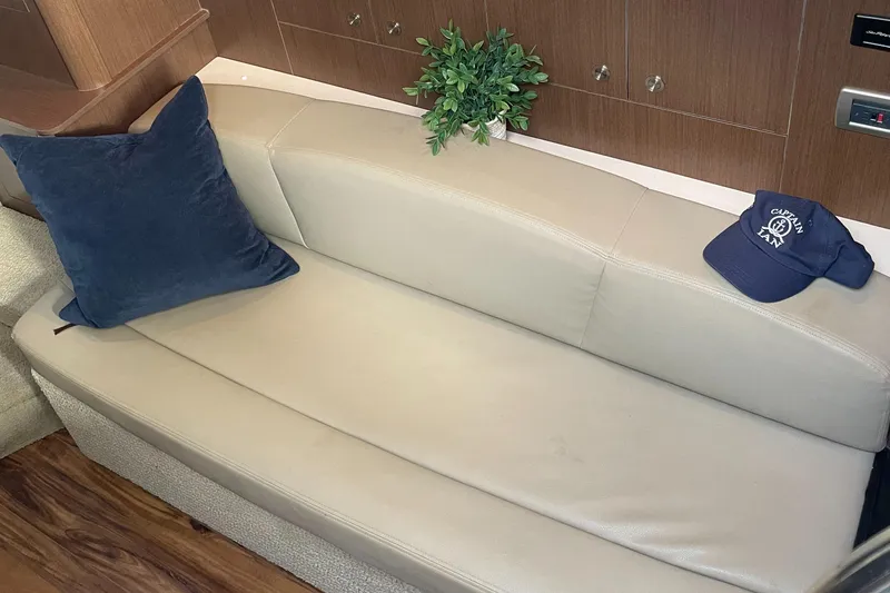 Slide: The Image of 2014 Sea Ray 330 Sundancer interior with beige leather seating, blue pillow, and cap. - 18