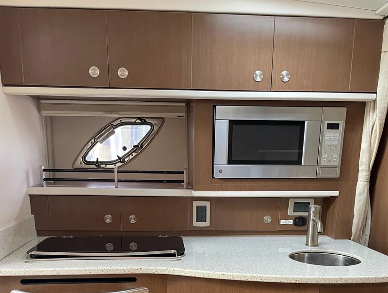 Slide: The Image of 2014 Sea Ray 330 Sundancer kitchen with microwave, sink, and porthole window. - 8