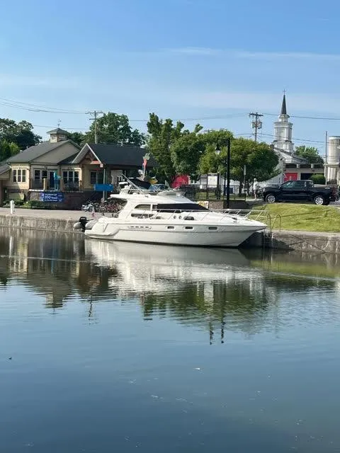 Slide: The Image of 1999 Sealine F44 yacht docked by a scenic waterfront with buildings and trees. - 2