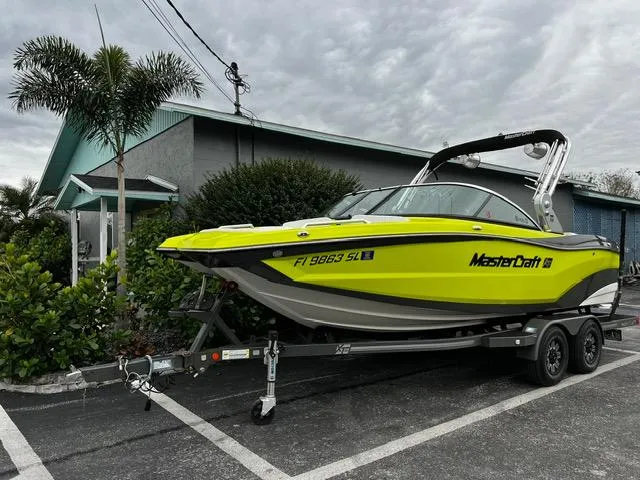 The Image of 2018 MasterCraft XT20 boat on trailer, parked near a house with palm trees. - 1