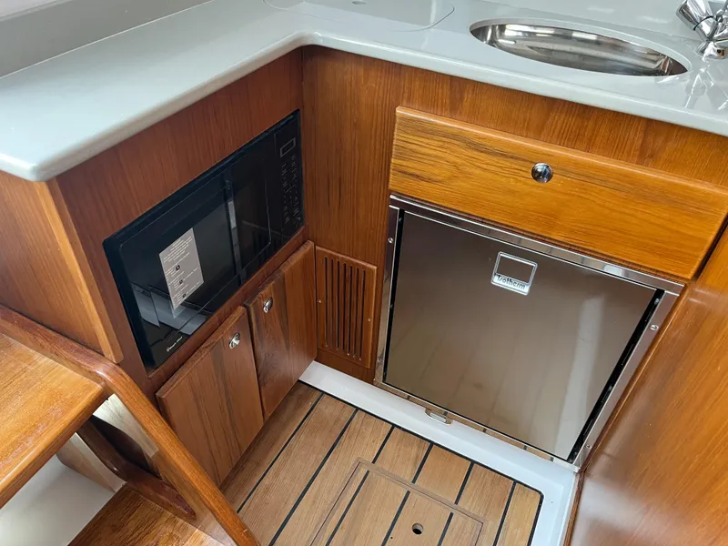 Slide: The Image of 2025 Southport 38 FE yacht interior with wood cabinetry, microwave, and stainless steel fridge. - 59