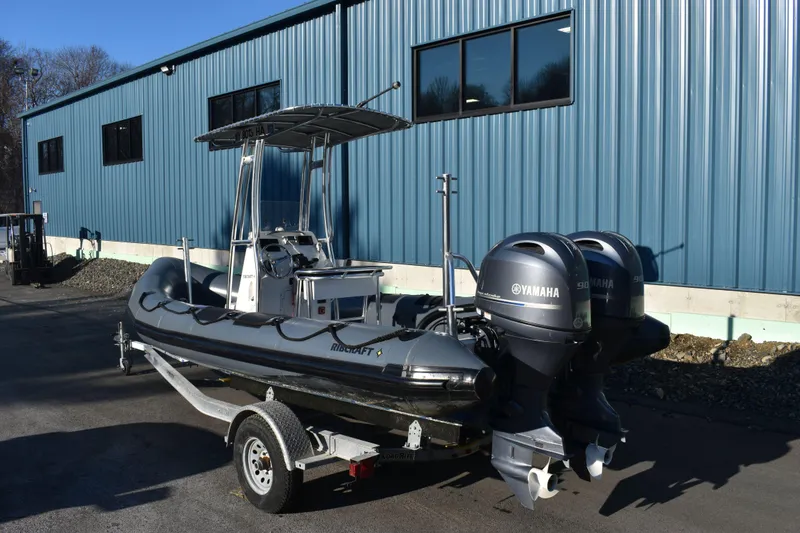 Slide: The Image of 2019 Ribcraft 6.5 boat with dual Yamaha engines on a trailer, parked by a blue building. - 4