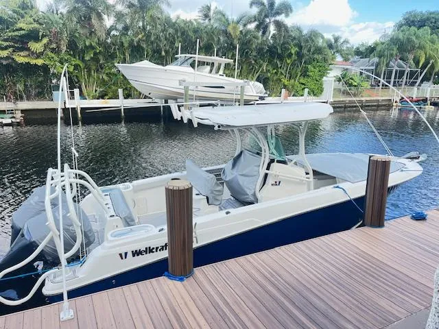 Slide: The Image of 2019 Wellcraft 262 F CC boat docked by a scenic waterfront with lush greenery. - 2