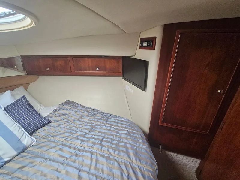 Slide: The Image of 2008 Riviera M470 yacht cabin with bed, wooden cabinets, and small TV. - 26