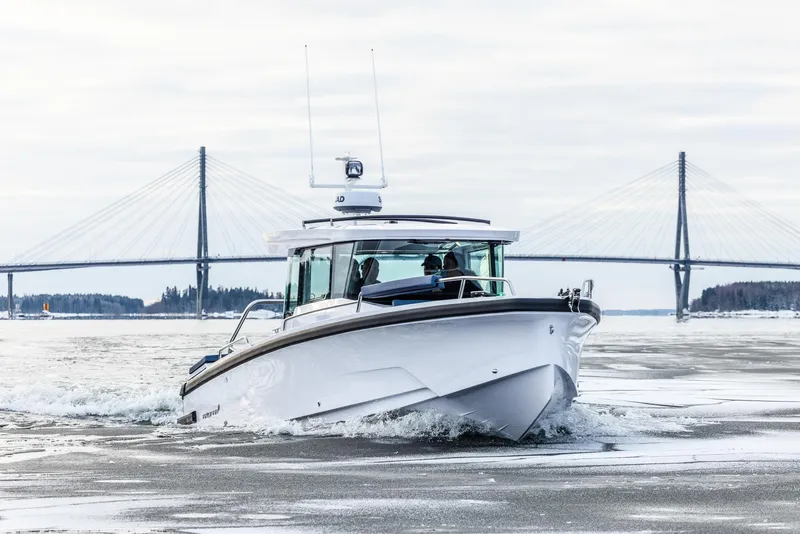 Slide: The Image of 2025 Axopar 29 XC Cross Cabin boat navigating icy waters near a bridge. - 2