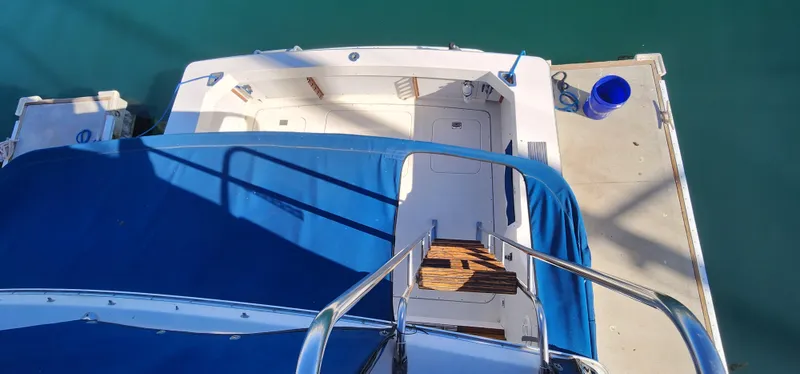 Slide: The Image of 1985 Bertram 33 Flybridge Cruiser docked, view from above, blue cover, wooden steps. - 10