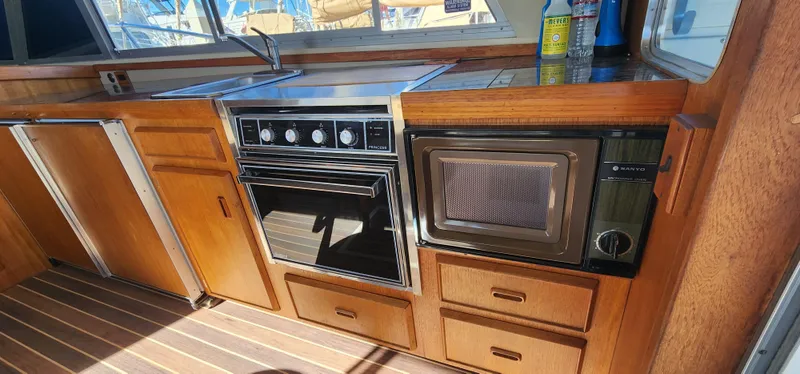 Slide: The Image of 1985 Bertram 33 Flybridge Cruiser kitchen with stove, microwave, and wooden cabinetry. - 15