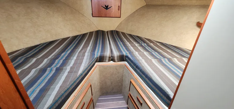 Slide: The Image of 1985 Bertram 33 Flybridge Cruiser cabin with striped bedding and wooden accents. - 19