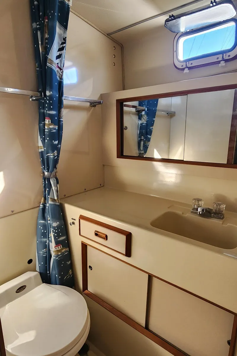 Slide: The Image of 1985 Bertram 33 Flybridge Cruiser bathroom with sink, mirror, and nautical-themed curtain. - 22