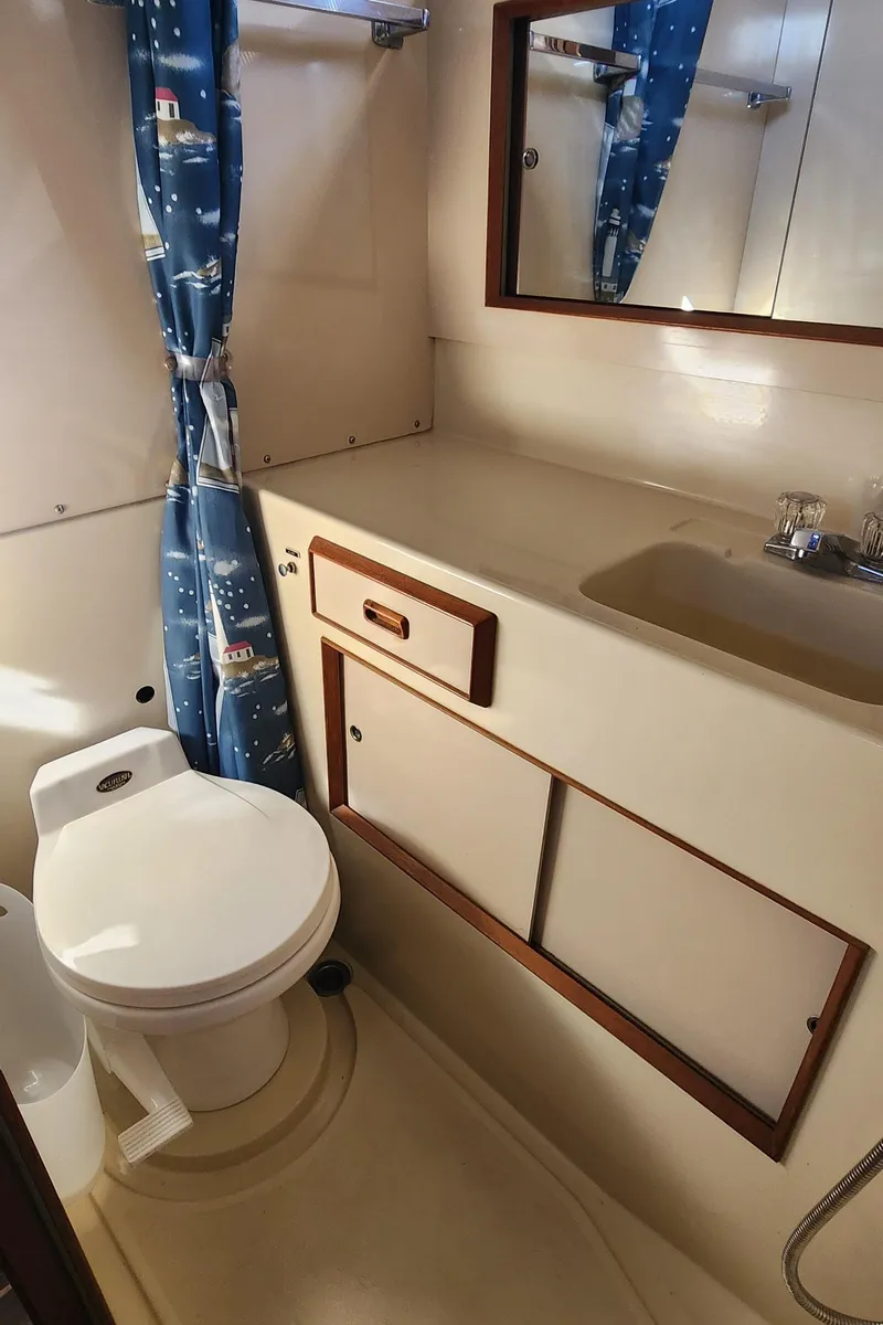 Slide: The Image of 1985 Bertram 33 Flybridge Cruiser bathroom with toilet, sink, and nautical-themed shower curtain. - 23