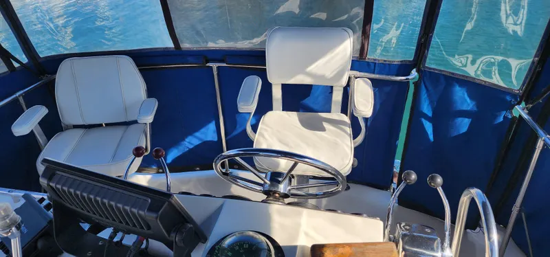 Slide: The Image of 1985 Bertram 33 Flybridge Cruiser helm with white seating and steering wheel. - 3
