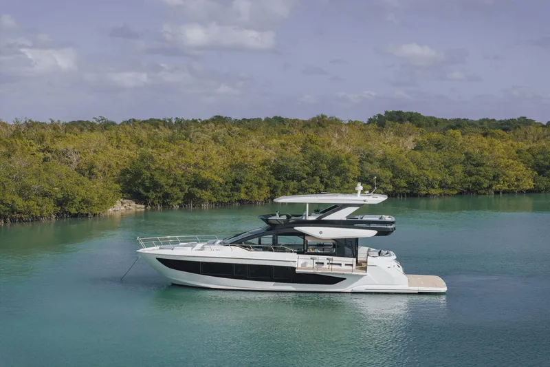 Slide: The Image of 2025 Cruisers Yachts 57 Fly on serene water with lush greenery backdrop. - 10