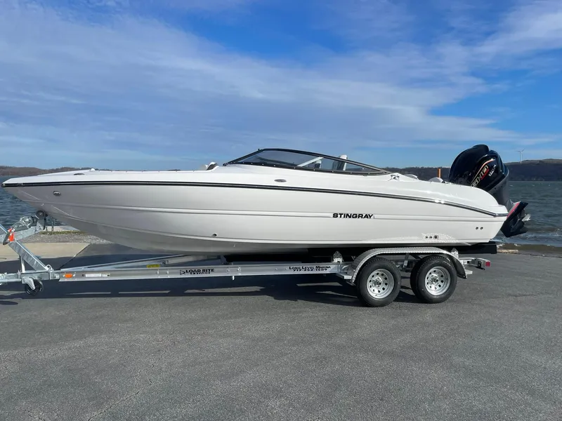 The Image of 2025 Stingray 23 OSX boat on trailer by the water, clear sky background. - 1