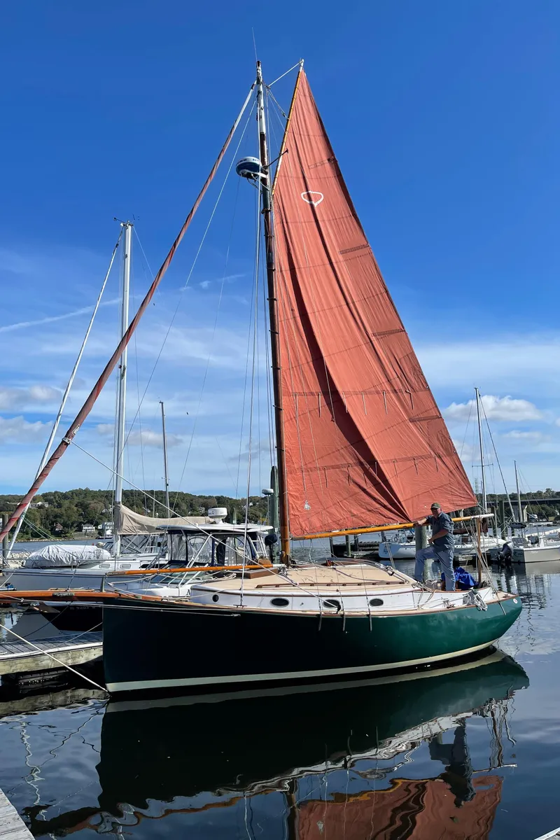 Slide: The Image of 1978 Legnos Mystic 30 sailboat with red sails docked at a marina under a clear blue sky. - 9