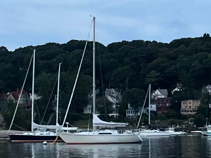 Slide: The Image of 1983 C&C 35 MKIII sailboat anchored in a scenic harbor with houses and trees. - 7