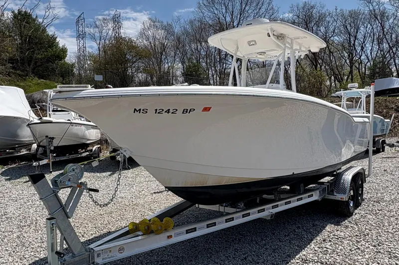 Slide: The Image of 2013 Tidewater 230 boat on trailer, parked on gravel, with trees in the background. - 5