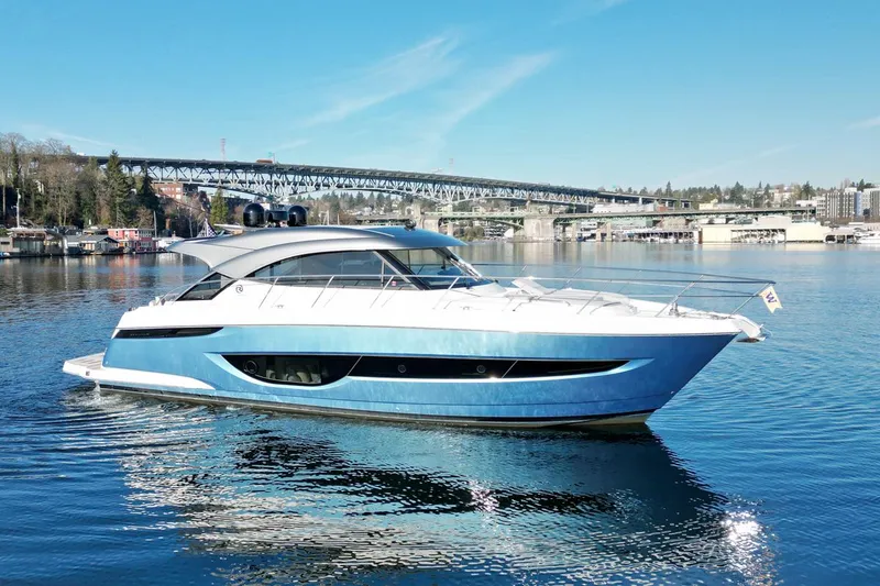 The Image of 2023 Riviera 4600 Sport Yacht Platinum Edition on serene water with bridge in background. - 0