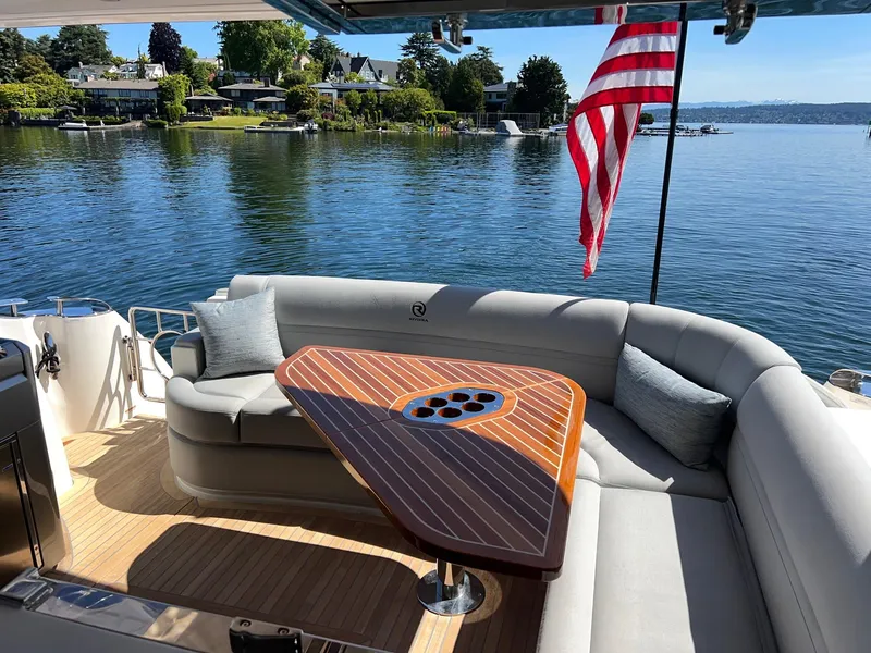 Slide: The Image of 2023 Riviera 4600 Sport Yacht Platinum Edition, luxurious deck with seating, table, and scenic waterfront view. - 4