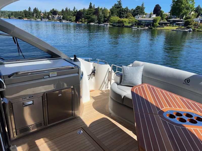 Slide: The Image of 2023 Riviera 4600 Sport Yacht Platinum Edition, luxurious deck with seating and scenic lake view. - 5