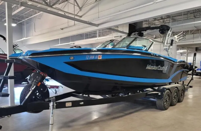 The Image of 2018 MasterCraft X26 boat on trailer in showroom, featuring sleek black and blue design. - 1