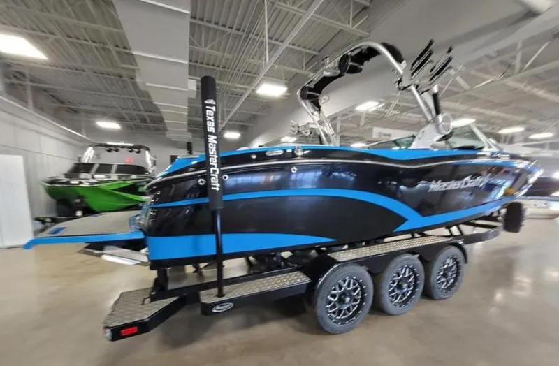 Slide: The Image of 2018 MasterCraft X26 boat in showroom, black and blue design, triple-axle trailer. - 14