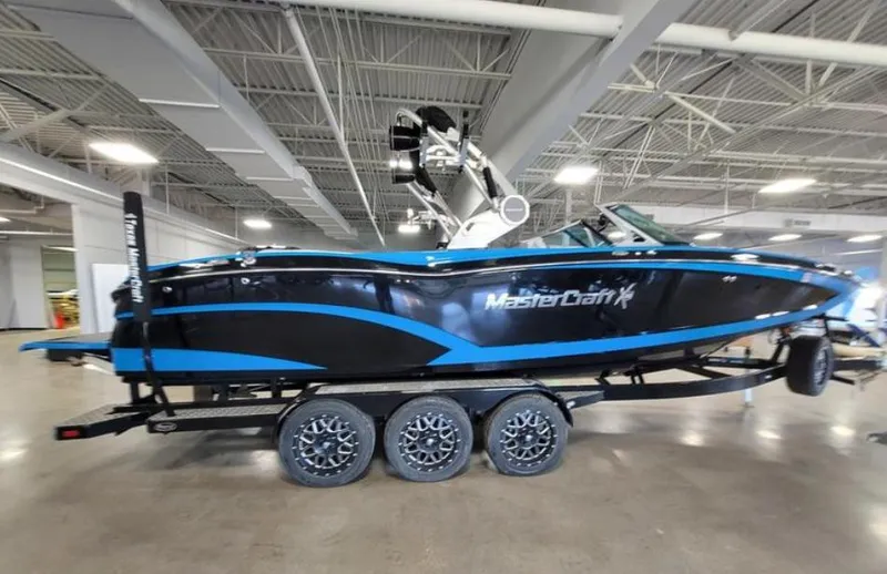 Slide: The Image of 2018 MasterCraft X26 boat with blue and black design on a triple-axle trailer indoors. - 15