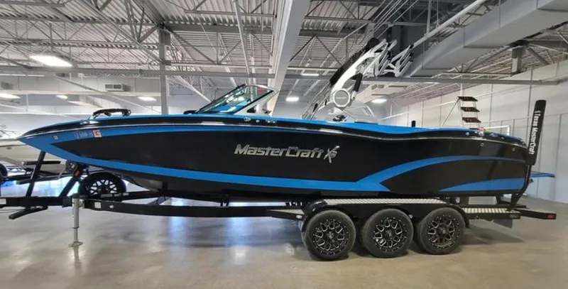 Slide: The Image of 2018 MasterCraft X26 boat on trailer in showroom, black and blue design. - 2