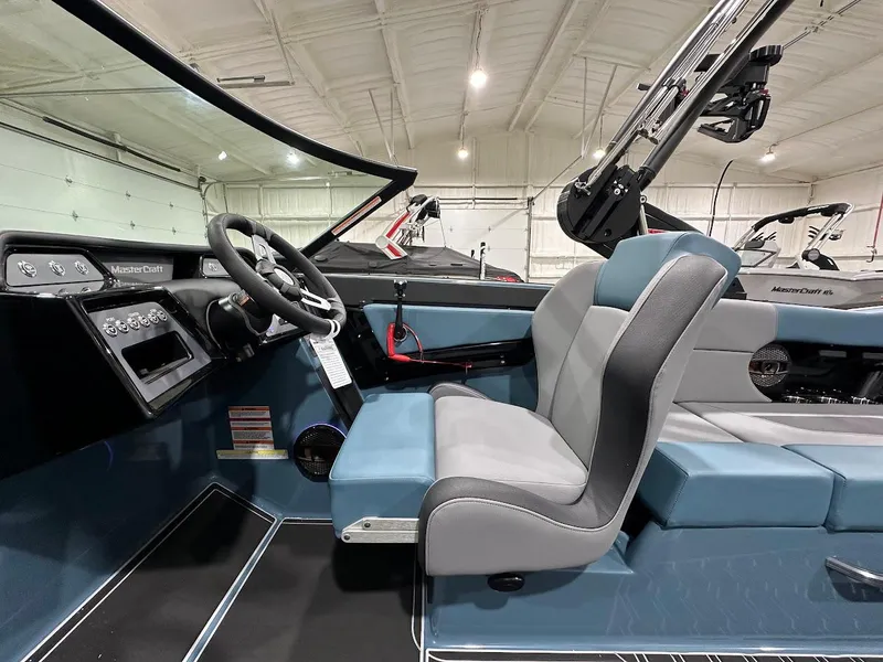 Slide: The Image of 2025 MasterCraft NXT23 boat interior with modern dashboard and comfortable seating in a showroom. - 11