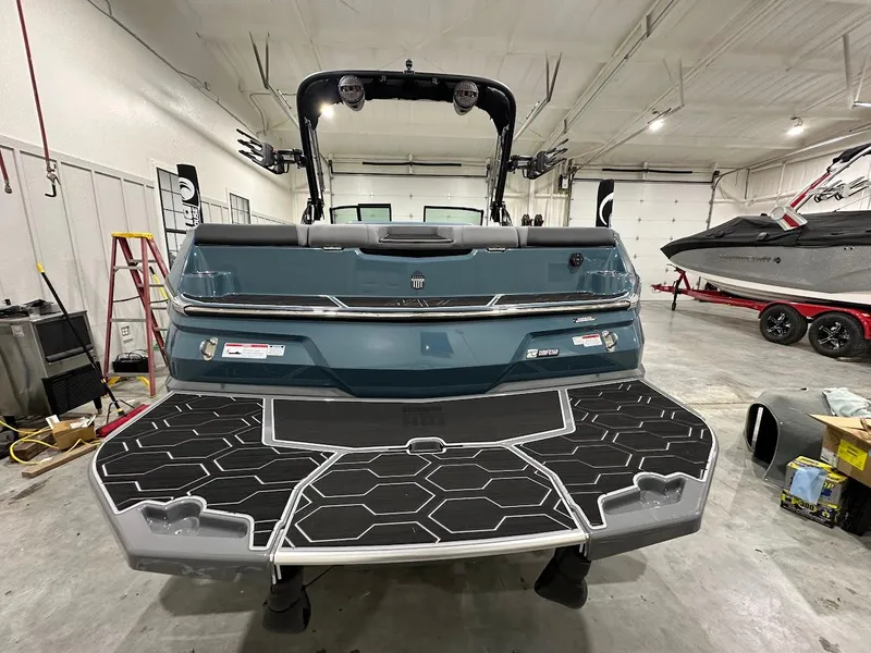Slide: The Image of 2025 MasterCraft NXT23 boat in a garage, rear view with swim platform. - 2
