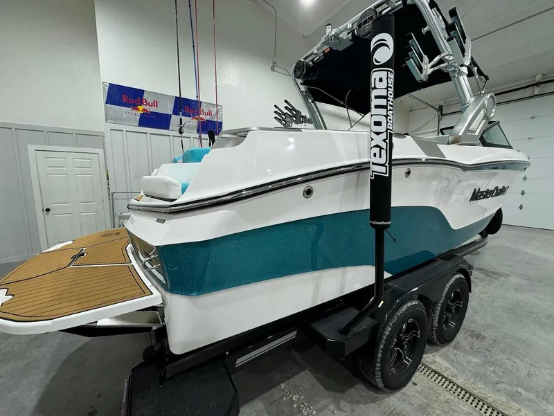 Slide: The Image of 2025 MasterCraft XT23 boat in garage, teal and white design, on trailer. - 16