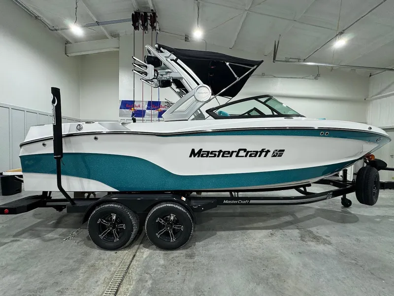 Slide: The Image of 2025 MasterCraft XT23 boat in showroom, white and teal design, on trailer. - 17