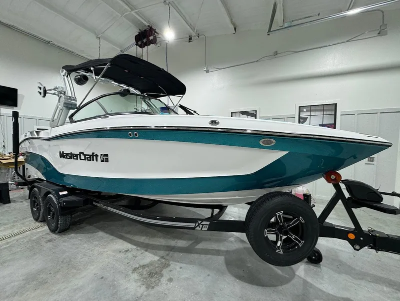 Slide: The Image of 2025 MasterCraft XT23 boat in a showroom, teal and white design on a trailer. - 18