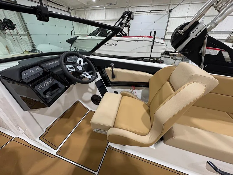 Slide: The Image of 2025 MasterCraft NXT24 boat interior with beige seating and modern dashboard in a showroom. - 12