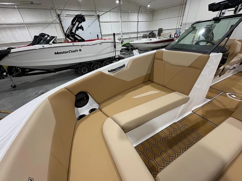 Slide: The Image of 2025 MasterCraft NXT24 boat interior with tan seating, hexagonal flooring, and sleek design in a showroom. - 15
