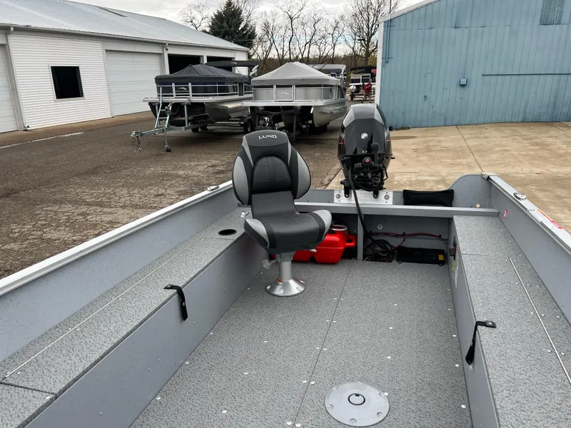 Slide: The Image of 2025 Lund 1600 Fury Tiller boat with seating and motor, parked near a warehouse. - 10