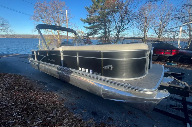 Slide: The Image of 2015 Manitou 25 Oasis SR pontoon boat parked near a lake, surrounded by autumn trees. - 0
